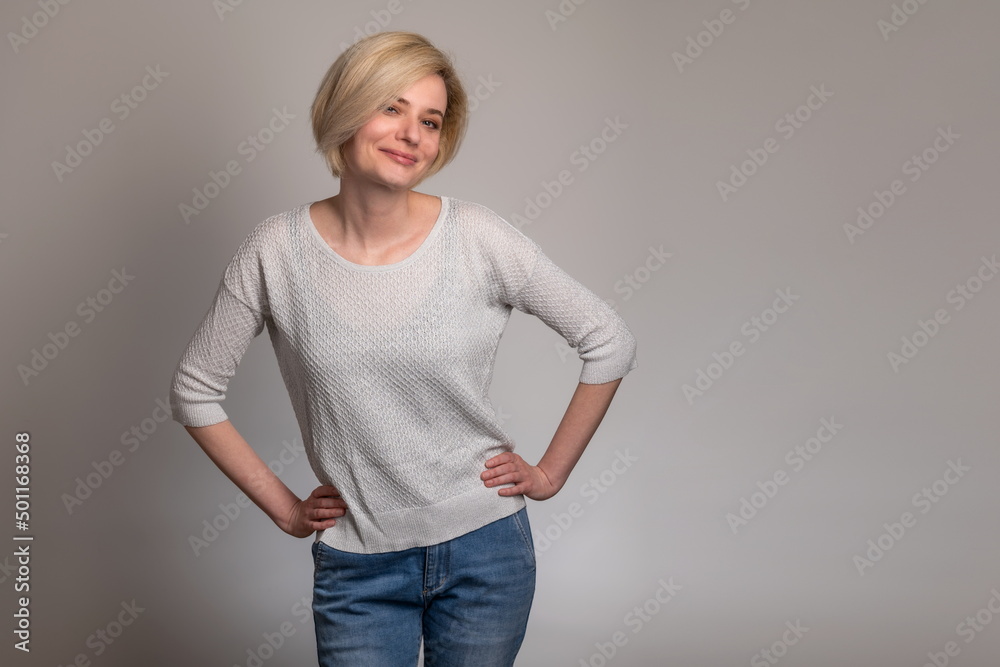 Smiling confidence. Beautiful young blonde women looking at camera and posing while standing against grey background