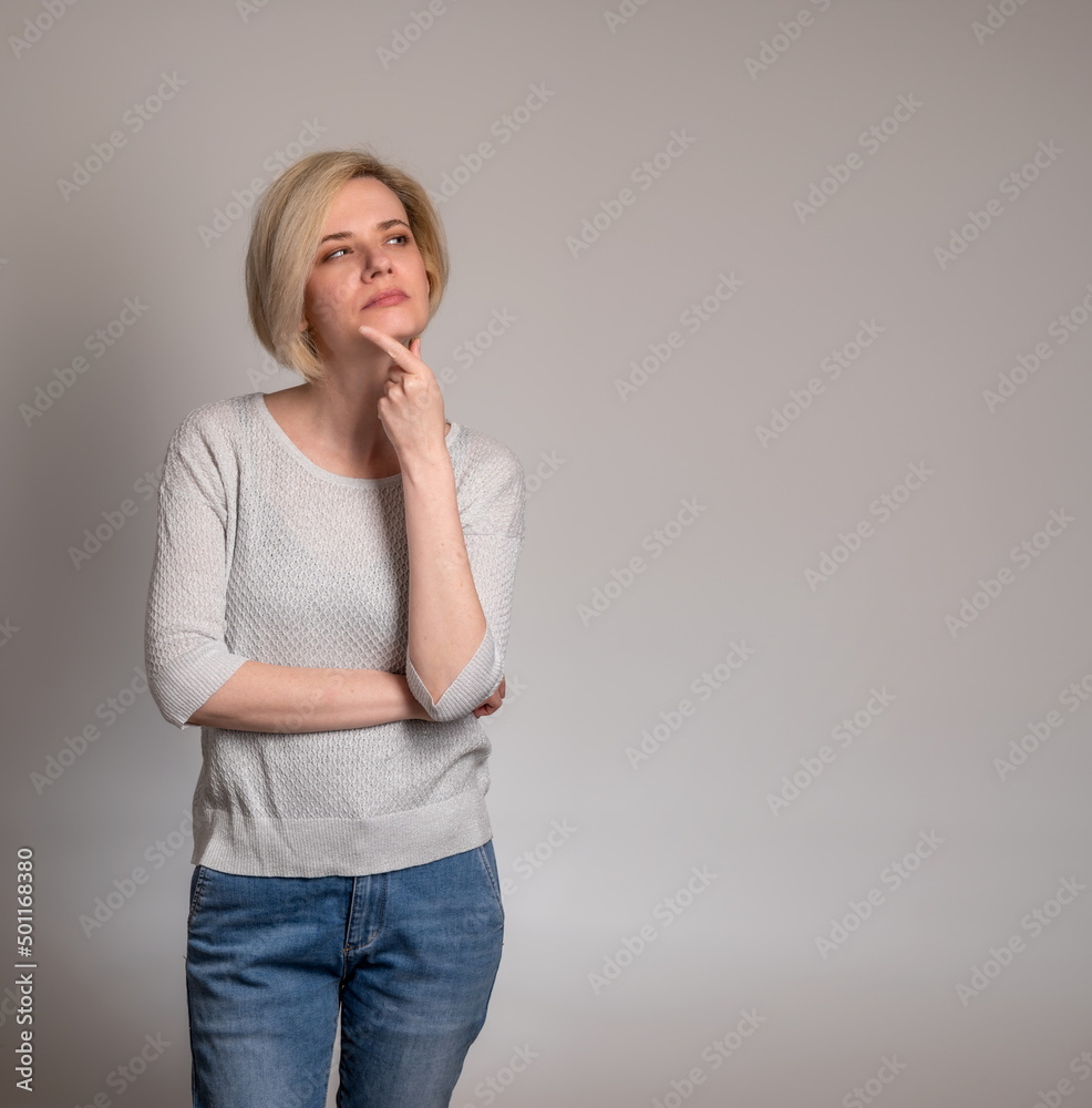 Thoughtful young woman, standin touching chin, looking aside at copy space, attractive female pondering deal, pensive client customer thinking about shopping offer, isolated on grey studio background