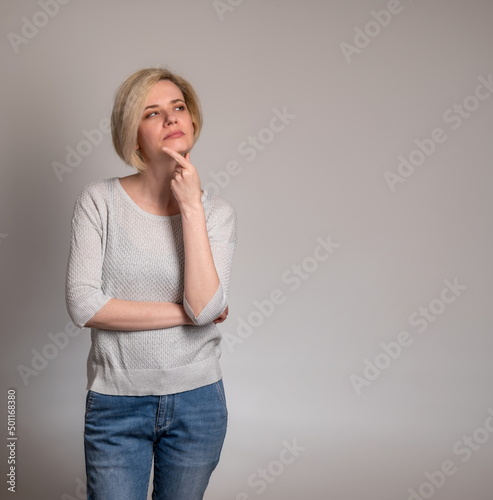 Obraz na płótnie Thoughtful young woman, standin touching chin, looking aside at copy space, attractive female pondering deal, pensive client customer thinking about shopping offer, isolated on grey studio background w salonie