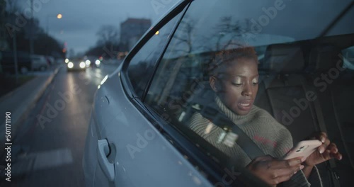 Young black woman passenger working on her mobile phoner while she is on the back seat of an uber taxi travelling through town photo