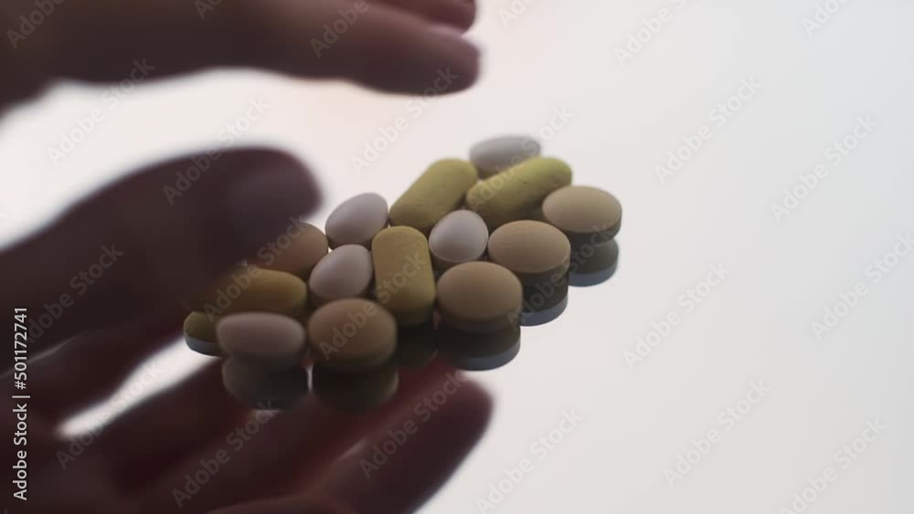 Hand laying bunch of pills on white table, then removes all except one