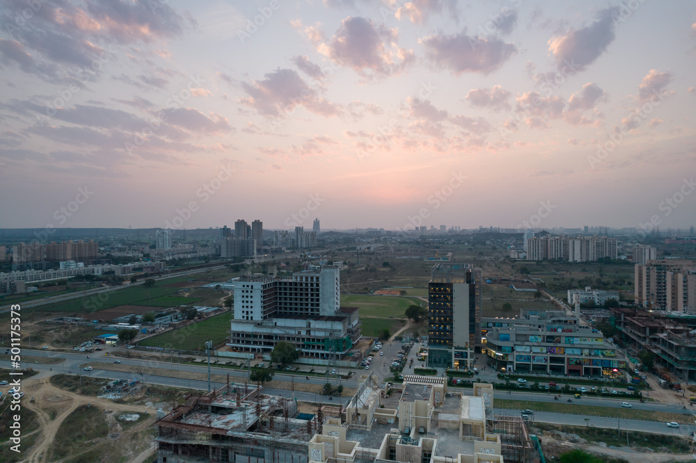Obraz premium aerial dusk shot showing 3 roads mall in gurgaon with lights switched on and traffic moving on the busy road in front and construction sites all around