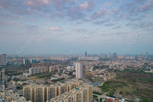aerial drone shot passing over a building with homes, offices, shopping centers moving towards skyscapers in front of sunset showing the empty outskirts of the city of gurgaon photo