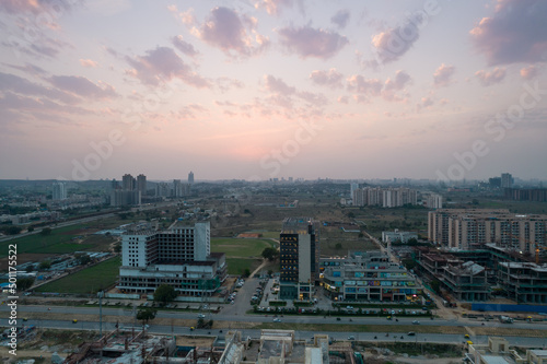 aerial dusk shot showing 3 roads mall in gurgaon with lights switched on and traffic moving on the busy road in front and construction sites all around