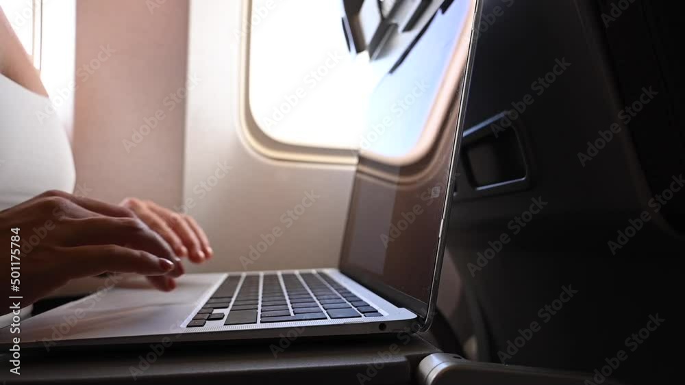Faceless woman in a mask works on a laptop on an airplane while sitting by the window during the flight. Freelancer on a journey. Faceless woman in a mask works on a laptop on an airplane while sitting by the window during the flight. Freelancer on a journey.