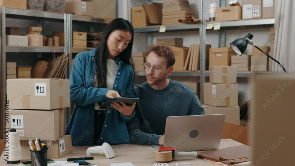Entrepreneurs checking order and typing some details at the tablet while preparing delivery parcel box at the warehouse. Post service and small business concept. Entrepreneurs checking order and typing some details at the tablet while preparing delivery parcel box at the warehouse. Post service and small business concept.