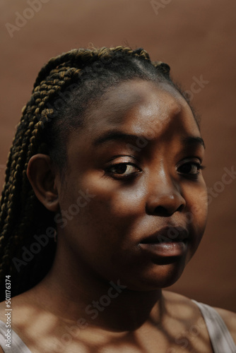 Close-up of African girl with natural beauty looking at camera against the brown background