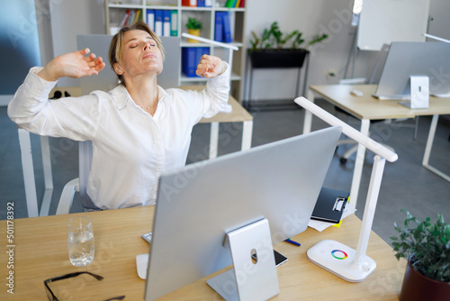 Middle aged business woman stretching at workplace in office