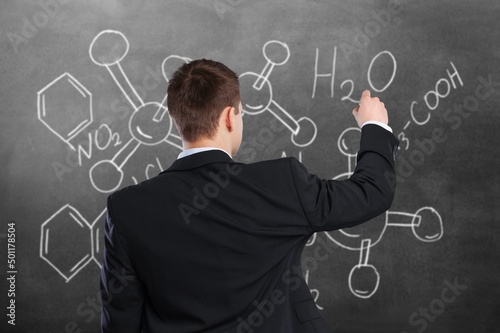 A smart scientist stands at the school blackboard explaining  scientific formulas