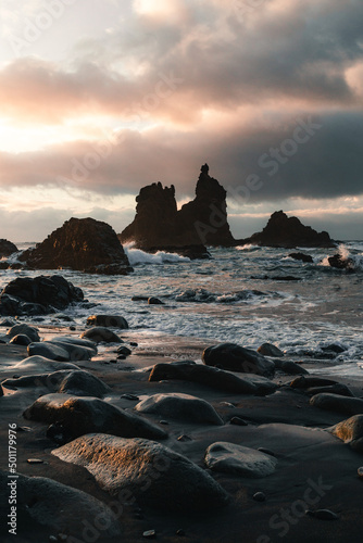 Beautiful view of beach with black sand and stones in North Tenerife coast at sunset. Atlantic wavy ocean with golden sun in Canary Islands. Dark photo of Playa de Benijo in Spain.