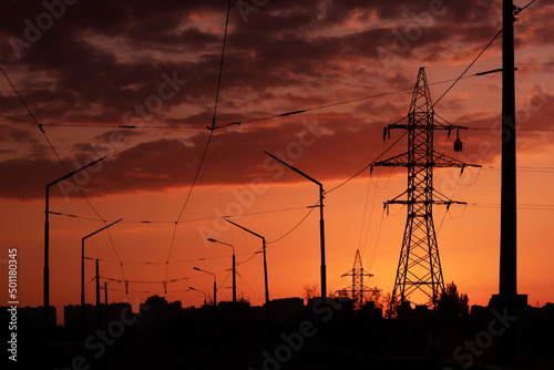 Fototapeta .black silhouettes of power line pylons, poles, wires and houses at sunset