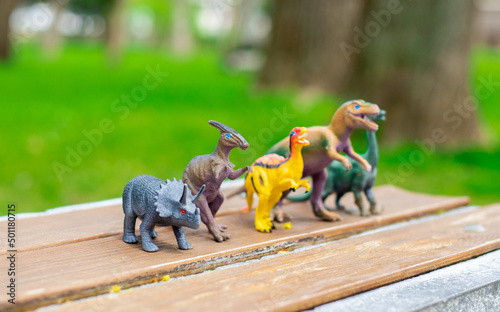 cute kid is playing with  dinosaurs toys on park bench  spring  green nature  grass. happy dinosaur day  may 15 and june 1. fascinating dinosaur fantasies. spring outside  public park having fun.