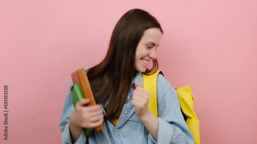 Beautiful smiling girl teen student hold books dance rest, wears shirt and yellow backpack, posing isolated over pink color background studio. Education in high school university college concept Beautiful smiling girl teen student hold books dance rest, wears shirt and yellow backpack, posing isolated over pink color background studio. Education in high school university college concept