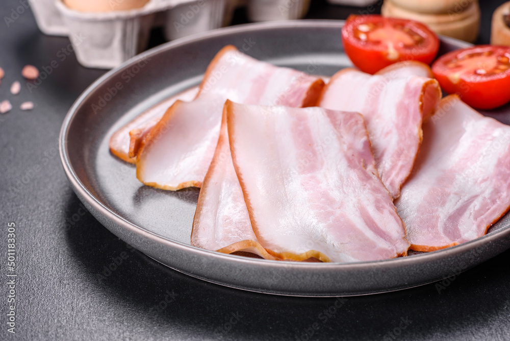 Delicious fresh raw bacon cut with slices on a grey plate against a dark concrete background