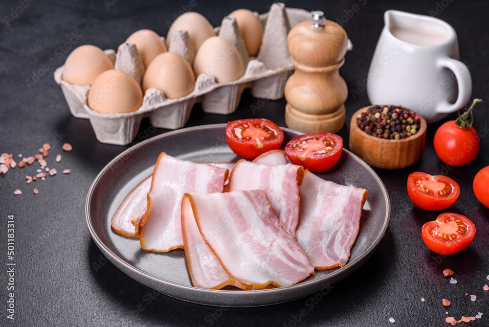 Delicious fresh raw bacon cut with slices on a grey plate against a dark concrete background Delicious fresh raw bacon cut with slices on a grey plate against a dark concrete background