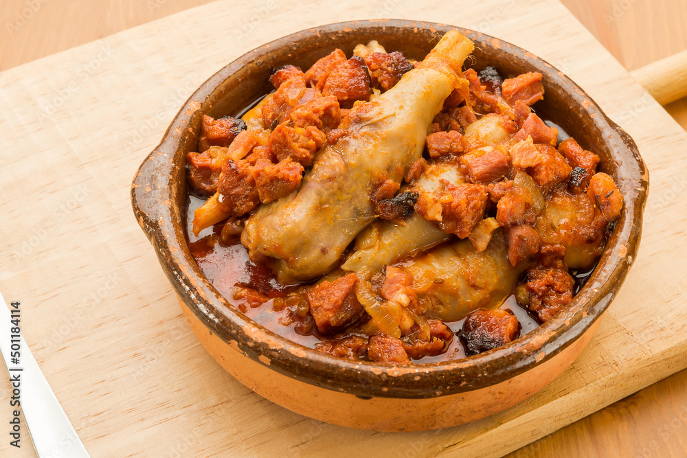 Typical Spanish food, lamb trotters with ham and chorizo. Horizontal view of food in a clay pot on a wooden table. Typical Spanish food, lamb trotters with ham and chorizo. Horizontal view of food in a clay pot on a wooden table.