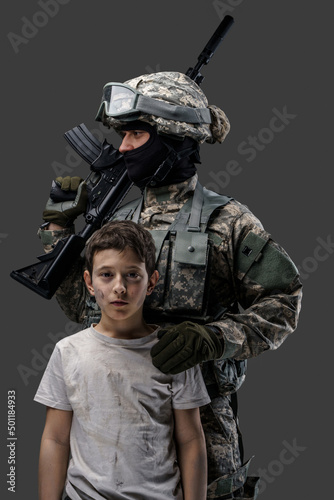 Soldier protecting little kid. Special force army man and young boy against gray background.