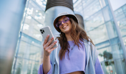Young cool girl holding and using mobile phone. Smiling woman texting with friends