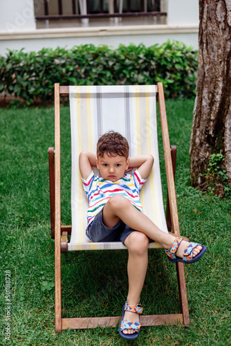 a laughing boy is lying on a folding chair on a chaise longue outside
