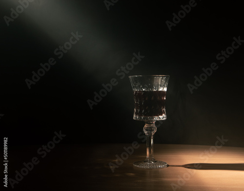 a beam of light illuminates a glass of blood in a dark room