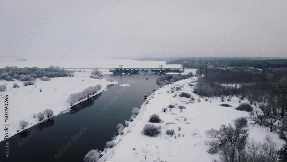 River in winter landscape with shore covered snow with hydroelectric dam on background, aerial view River in winter landscape with shore covered snow with hydroelectric dam on background, aerial view