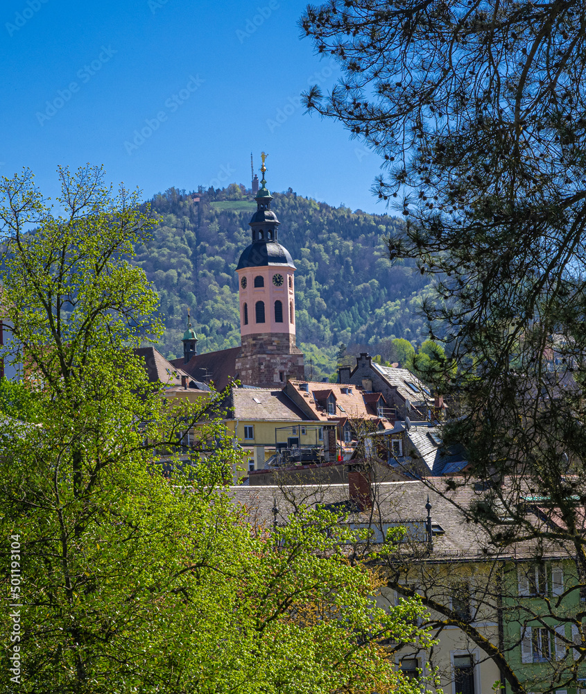 The steeple of the collegiate church in Baden Baden in the background the Merkur mountain. Baden Wuerttemberg, Germany, Europe The steeple of the collegiate church in Baden Baden in the background the Merkur mountain. Baden Wuerttemberg, Germany, Europe