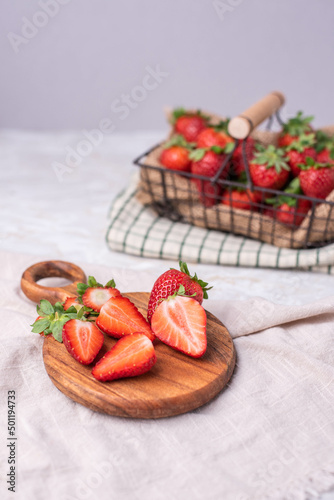 Erdbeeren im Drahtkorb auf einem Tisch mit Holzbrett und geschnittenen Erdbeeren