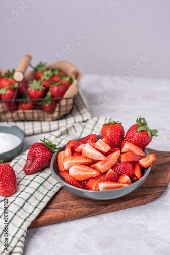 Schale mit geschnittenen Erdbeeren auf einem Brett und einer kleinen Schale Zucker  Korb mit frischen Fr  chten