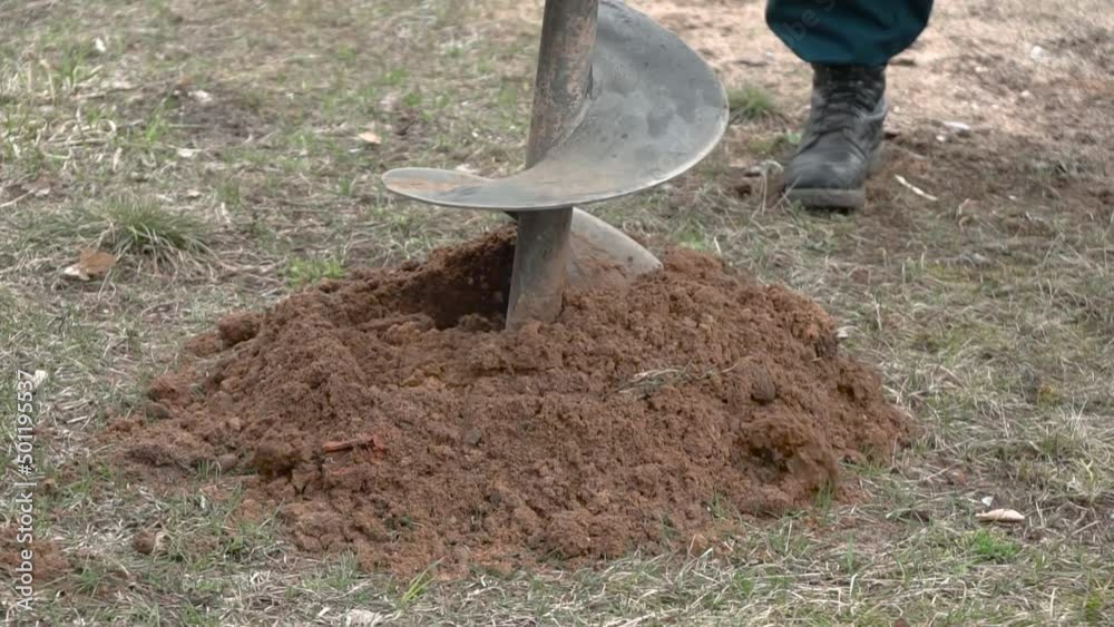Drill bit for drilling soil close up. Drilling a hole into ground at a construction site. Tractor drill the ground. Male worker building pile foundation for wooden frame house or planting trees