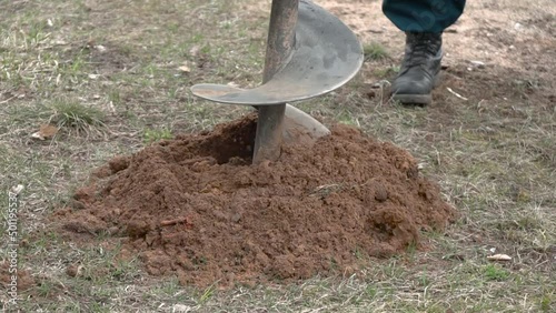 Drill bit for drilling soil close up. Drilling a hole into ground at a construction site. Tractor drill the ground. Male worker building pile foundation for wooden frame house or planting trees