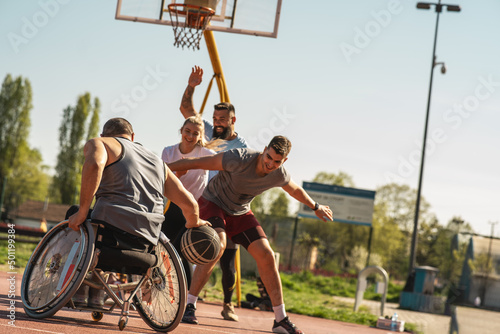 A physically challenged man in a wheelchair fearlessly engages in a spirited game of basketball with his supportive friends, breaking barriers and proving that passion and teamwork know no bounds.		 photo