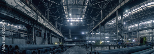 Panoramic photo of large dark warehouse workshop in factory for production metal pipes.