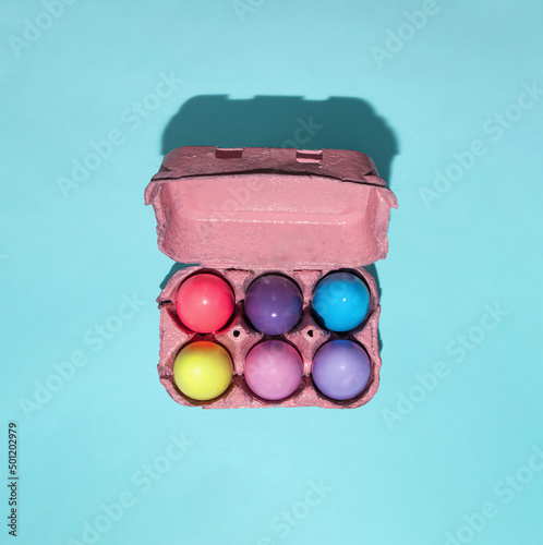 Colorful pastel eggs in carton on light blue background. Creative minimalistic Easter concept. photo