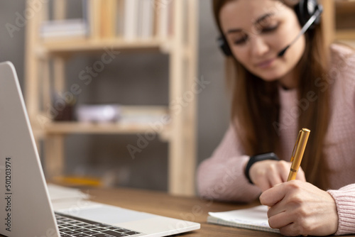 Girl listen headphones and writing on notepad. Student woman online larning