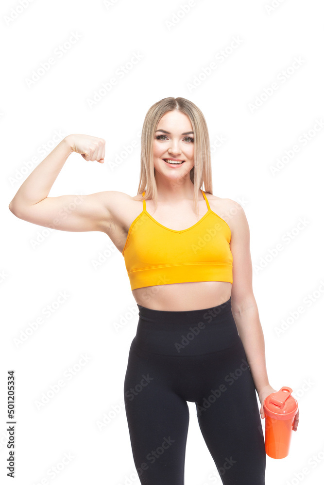 A beautiful, athletic, slim, smiling and cheerful woman in an orange top and black sweatpants in a comic form demonstrates her bicep muscles and holds a bottle of water. Lifestyle concept with sports A beautiful, athletic, slim, smiling and cheerful woman in an orange top and black sweatpants in a comic form demonstrates her bicep muscles and holds a bottle of water. Lifestyle concept with sports