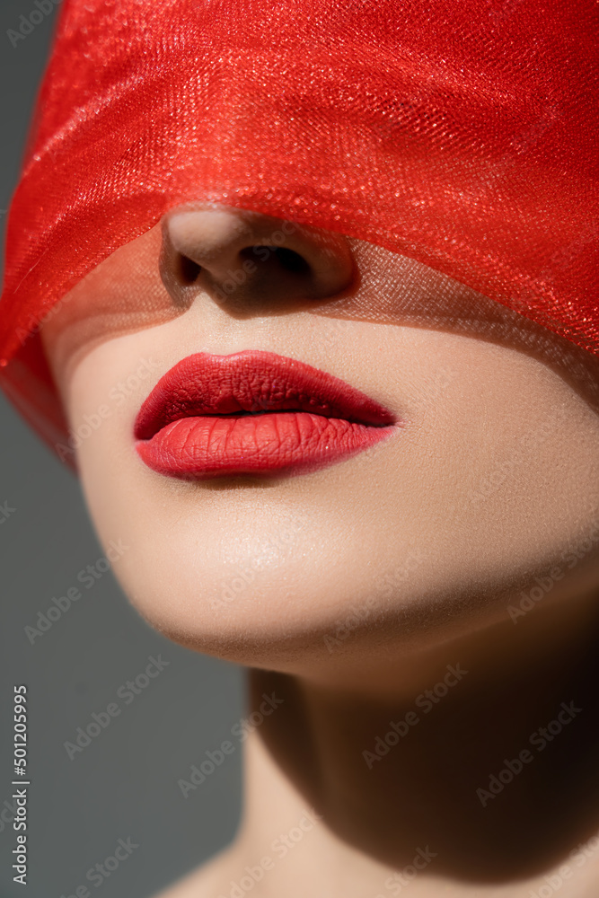 Close up view of woman with red cloth on face standing isolated on grey.