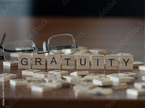 gratuity word or concept represented by wooden letter tiles on a wooden table with glasses and a book photo