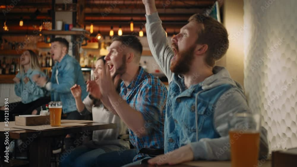 A group of men and women in a pub together cheer for their national team at the World Cup in football, basketball, hockey. Celebrate the goal scored, the puck A group of men and women in a pub together cheer for their national team at the World Cup in football, basketball, hockey. Celebrate the goal scored, the puck