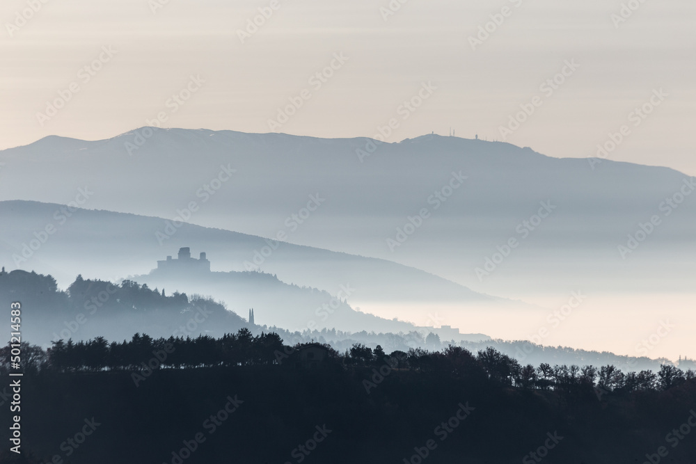 Mist and fog between valley and layers of mountains and hills in Umbria Italy with Assisi silhouette at the distance