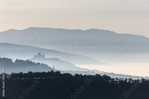 Mist and fog between valley and layers of mountains and hills in Umbria Italy with Assisi silhouette at the distance