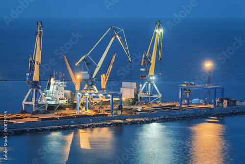 Sea commercial port at night in Mariupol, Ukraine before the war. Industrial. Cargo freight ship with working cranes bridge in sea port at twilight. Cargo port, logistic. Heavy industry photo