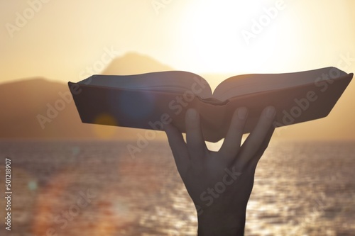 Hand holding open bible book up to the sun light.