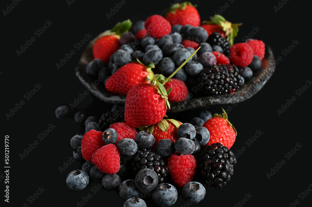 Assorted fresh berries in a bowl on black background Assorted fresh berries in a bowl on black background
