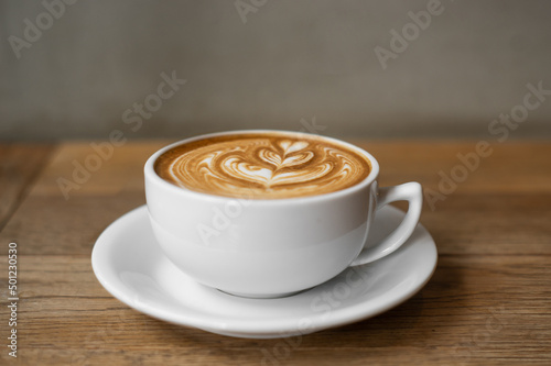 Hot coffee cup with milk late art foam on wood background