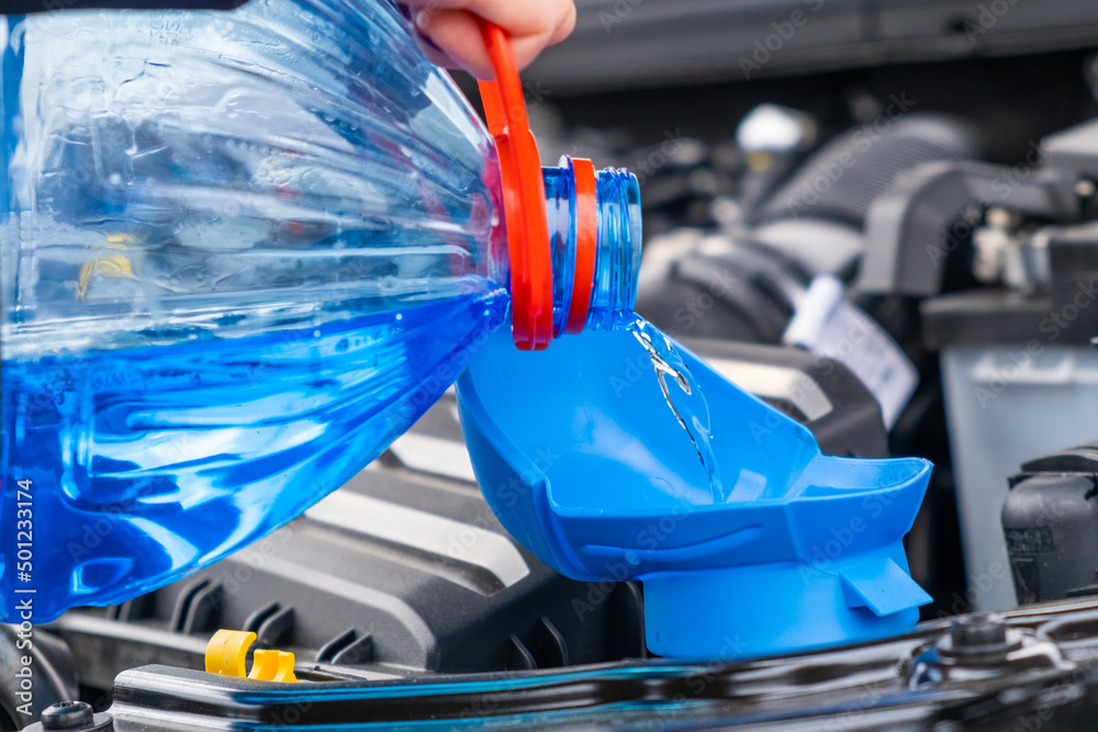 Close up driver pouring blue non freezing windshield glass washer fluid