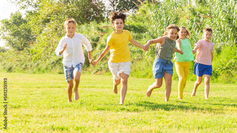 Group of five happy children who are jogging in a park on a sunny day