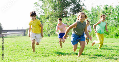 Group of school children, boys and girls, laughing and running in a city park at summer day