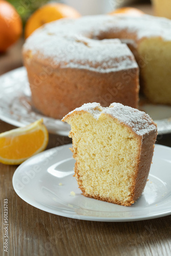 Close up piece of moist orange fruit cake on plate with orange slices on wooden table. Delicious breakfast, traditional English tea time. Orange cake recipe.