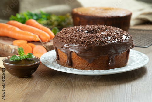 Brazilian carrot cake with chocolate frosting on wooden table with carrots in the background