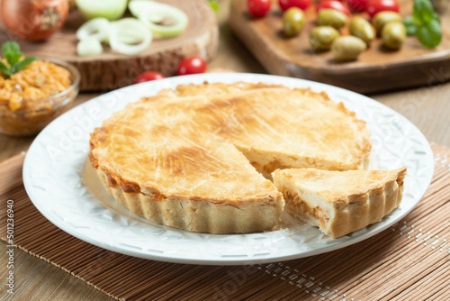 Chicken pie with cottage cheese, tomatoes, onion and olives on wooden table and white plate.